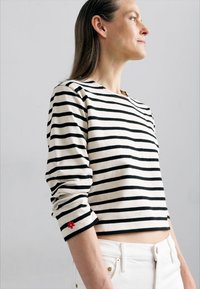 Striped cotton long-sleeve shirt with black and cream horizontal lines, cropped design, and red floral embroidery on sleeve cuff.