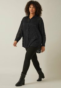 Black, long-sleeve shirt with a sheer, textured design and button front. Paired with black skinny pants and heeled ankle boots.
