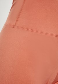 Leggings atletici leggeri di un colore corallo con una texture liscia e dettagli cuciti, che mostrano un design aderente.