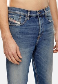 Džínové kalhoty ve světle modré barvě s bledým povrchem. Mezi vlastnosti patří přední kapsa s etiketou, uzávěr na knoflík a kontrastní šití.