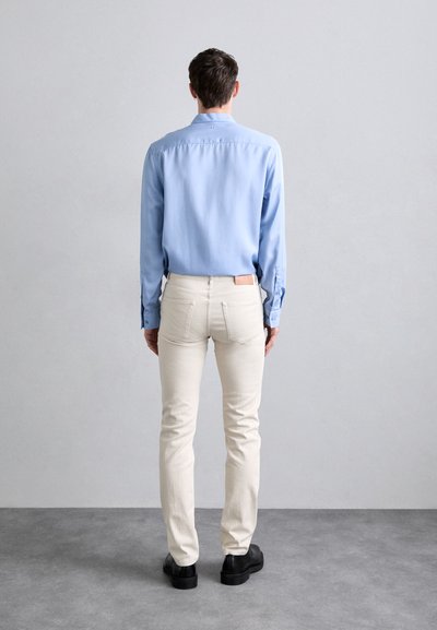 Light blue button-up shirt, cream-colored fitted pants, and black shoes. Simple design, smooth fabric, and a slight sheen on the shirt.