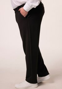 Pantalones negros de tejido suave, con bolsillos laterales, un corte relajado y combinados con zapatillas blancas. Detalle limpio en la cintura visible.
