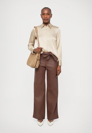 Camisa de satén beige, pantalones de tiro alto de pierna ancha marrones con un lazo, y tacones crema de punta. Acentuado con un bolso de hombro en tono marrón.