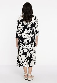 Sort-hvid blomsterkjole med trekvartærmer og en svævende design, parret med lyse sandaler med stroppelukning.