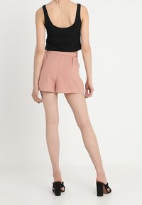 Černý top bez rukávů kombinovaný s růžovými kraťasy s vysokým pasem, které mají hladkou texturu a zipové zapínání, doplněný černými platformovými sandály.