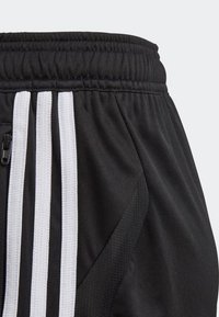 Pantalones cortos deportivos negros hechos de una tela suave, con una cintura elástica y un bolsillo con cremallera. Presenta tres rayas blancas en el costado.
