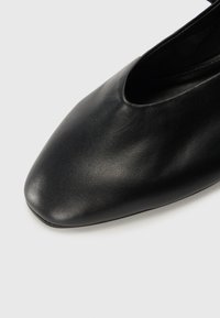 Čierna kožená obuv s špicatou špičkou a výrezom na vrchu. Hladká textura a minimalistický dizajn, žiadne viditeľné kovové prvky alebo akcenty.