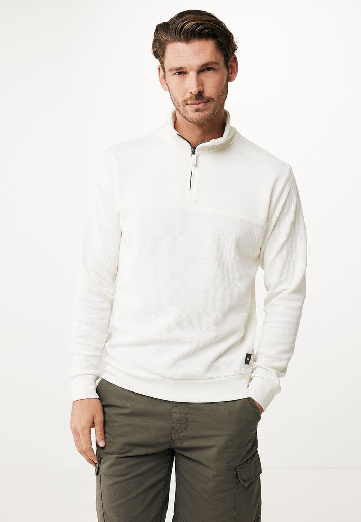 Vit zip-up sweatshirt i textured tyg, med en liten svart dragkedja och ribbade muddar. Kombinerad med gröna cargobyxor.