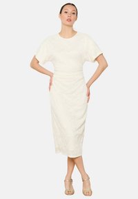 Floral lace midi dress in ivory with a round neckline, short wide sleeves, and a fitted waist, paired with strappy gold heels.