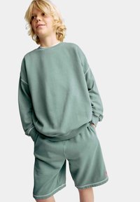 Lys grøn sweatshirt og matchende shorts i blødt stof, der har en afslappet pasform og synlige syninger.