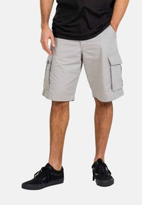 Hellegraue Cargo-Shorts mit zwei Seitentaschen und umgeschlagenen Säumen, aus einem leichten Stoff gefertigt. Kombiniert mit schwarzen Schnürsneakern.
