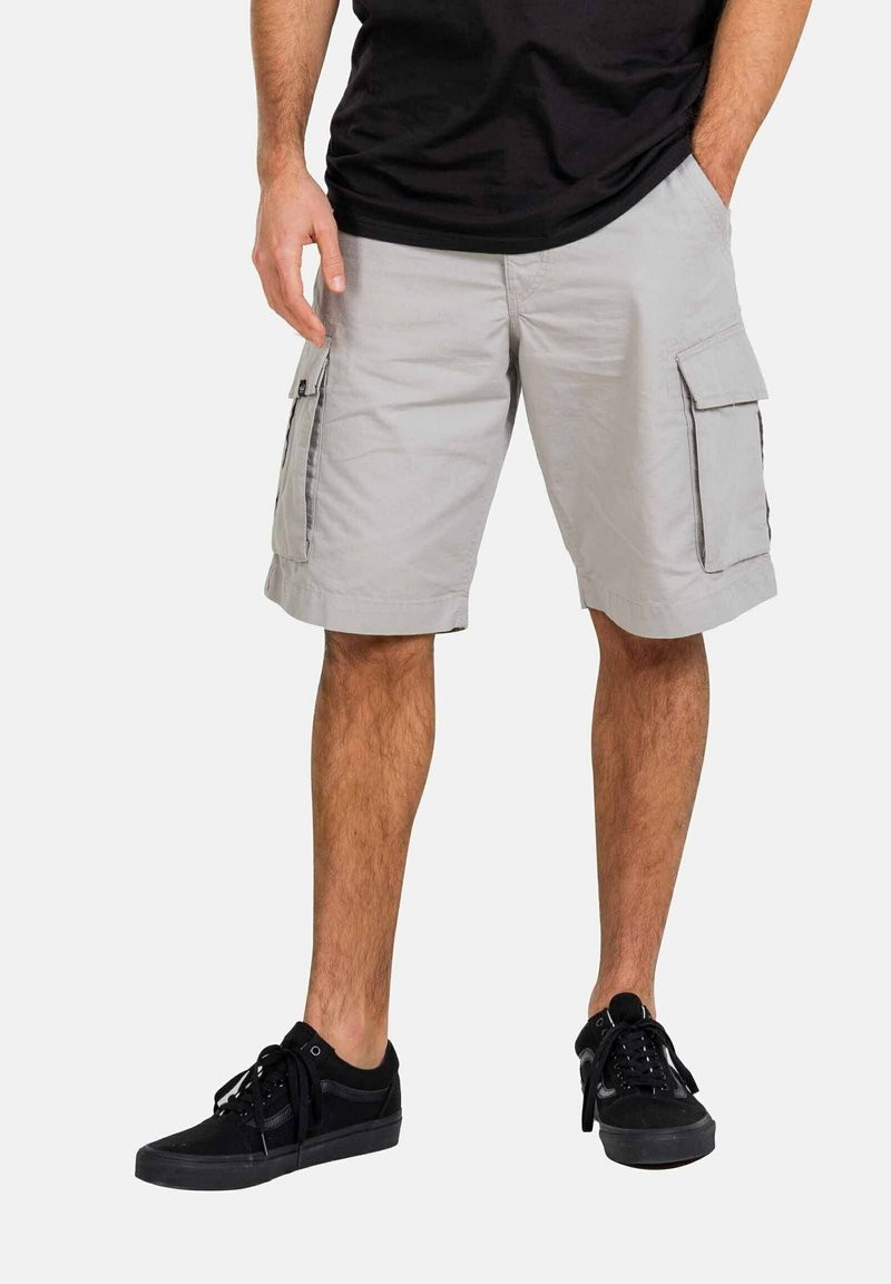 Hellegraue Cargo-Shorts mit zwei Seitentaschen und umgeschlagenen Säumen, aus einem leichten Stoff gefertigt. Kombiniert mit schwarzen Schnürsneakern.