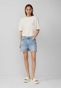Witte t-shirt met korte mouwen gecombineerd met lichtblauwe denim shorts met opgerolde manchetten en versleten accenten; lichtgekleurde chunky slide sandalen.