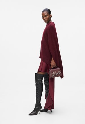 Burgundy oversized sweater, layered with a burgundy skirt. Black thigh-high boots and a small maroon handbag with silver logo detail.