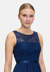 Robe bleu marine avec un corsage en dentelle à motifs floraux, un col festonné et une ceinture en satin lisse.
