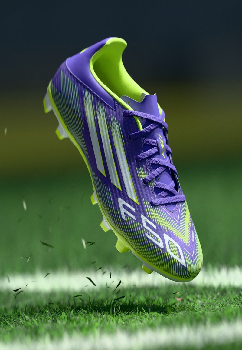 Crampons de football violet et vert lime avec un design texturé, comportant trois rayures blanches et un profil léger. Semelle extérieure à crampons.