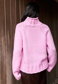 Rózsaszín kötött pulóver magas nyakkal, bordázott szegéllyel és leengedett vállakkal. A texturált anyag puha, bolyhos megjelenésű.