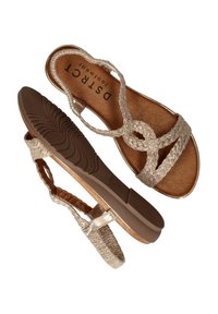 Vlechteen metallic gouden sandalen met een platte bruine zool en gestructureerde banden. De binnenzool heeft een gladde, shimmerende tan kleur.