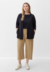 Navy cardigan with three-quarter sleeves, pockets, paired with beige wide-leg trousers and white sneakers on a neutral background.