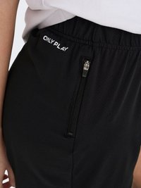 Pantalon noir à taille élastique avec poche zippée et logo blanc "ONLY PLAY", porté avec un haut blanc, montrant une partie de la main et du bras d'une personne.