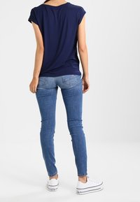 Marinblå kortärmad topp, avslappnad passform, kombinerad med ljusblå skinny jeans och vita canvas sneakers. Enkel, avslappnad outfit.