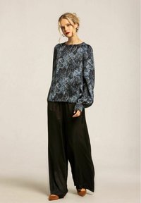 Blå blommig mönstrad blus med långa ärmar, mjuk textur; kombinerad med svarta höga byxor med vida ben och bruna platta skor.