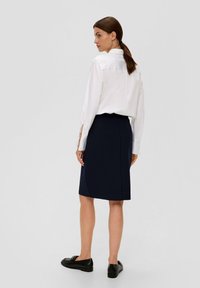 Weißes Hemd mit langen Ärmeln, mit Rückenfaltendetail, kombiniert mit einem knielangen, marineblauen Bleistiftrock und schwarzen Loafers.