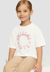 Weißes Baumwoll-T-Shirt mit einer pinken Grafik, auf der "AWESOME LOVE" steht, umgeben von kleinen Herzformen. Das Modell trägt beigefarbene, gefalte Hosen.