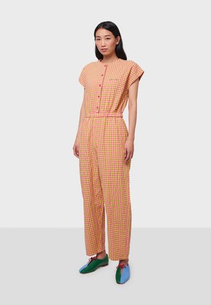 Combinaison à motif vichy rose et jaune, à manches courtes, avec un devant à boutons, une taille élastique et des jambes larges. Modèle portant des chaussures bicolores.