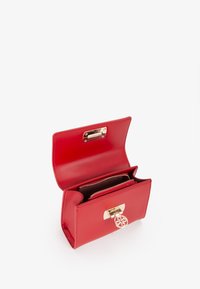 Sac à main en cuir rouge avec un design épuré, doté d'un fermoir doré et d'un pendentif décoratif. L'intérieur comprend plusieurs compartiments zippés.