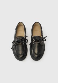 Zapatos de cuero negro con punta redonda, costuras decorativas y cordones. Presentan un diseño minimalista y suelas de goma.