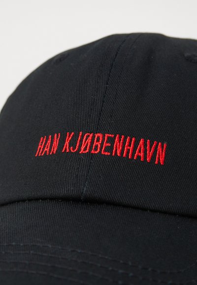 Căciulă de baseball neagră cu text brodat roșu "HAN KJØBENHAVN" pe față. Prezintă o formă structurată și un material texturat.