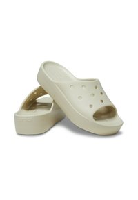 Zoccoli beige realizzati in plastica leggera, con design aperto sulla punta, fori di ventilazione e una soletta strutturata. Suola piatta con un sottile dettaglio del logo.