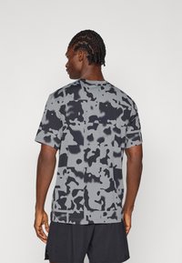 Lühikese varrukaga t-särk, millel on hall ja must kamuflaažimuster, valmistatud tekstureeritud kangast, ümar kaelus ja vabalt langev lõige.