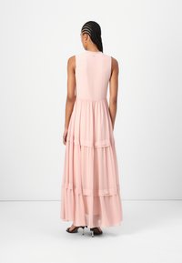 Abito lungo senza maniche di colore rosa con design a strati, realizzato in tessuto leggero. Presenta una silhouette svasata e una chiusura con bottone sul retro.