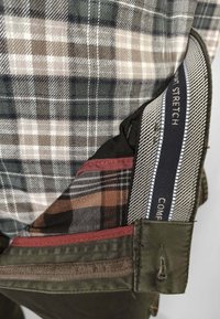 Pantaloni a quadri marroni e verde oliva in tessuto elasticizzato, con più fodere per tasche di diverse trame e colori, tra cui bordeaux e blu navy.