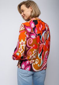 Langärmlige Bluse mit einem lebhaften Blumenmuster in Orange, Pink und Türkis auf einem hellen Hintergrund. Hergestellt aus glattem Stoff mit einer lässigen Passform.