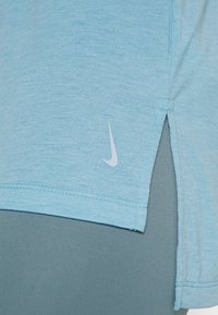 Ljusblå idrottströja med lätt textur, sidofledningar och en liten vit Nike-logotyp på nedre högra sidan.