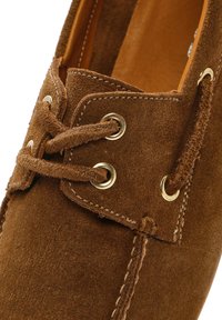 Bruine suède boot schoen met gouden oogjes en bruine veters; heeft contrasterende stiksels en een gladde binnenvoering.