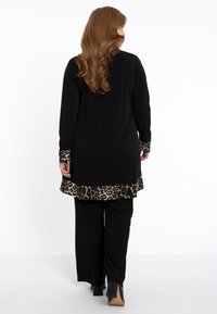 Zwarte tuniek met een broek met luipaardprint aan de onderrand en mouwen, gecombineerd met zwarte broeken. De outfit heeft een ontspannen pasvorm en een zachte stoftextuur.