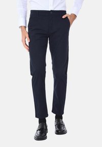 Chino navy in cotone con una vestibilità slim. Presenta una parte frontale liscia, passanti per cintura e tasche laterali. Indossati con mocassini neri.
