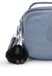 Borsa in nylon blu con superficie testurizzata e chiusura a zip. Include un portachiavi a forma di gorilla nero in peluche e una tracolla intrecciata con un accento marrone.