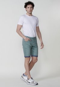 Shorts en jean bleu clair avec des ourlets roulés, poches avant et texture lisse, associés à un t-shirt blanc uni et des baskets sportives.