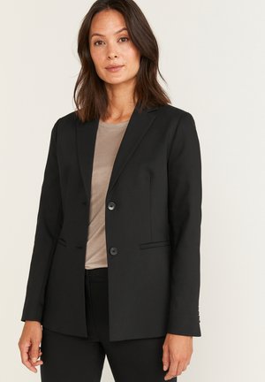 Svart kavaj med skräddarsydd passform, två knappar och sidfickor. Slät tyg, getinglappar och lång ärm. Bärs över en beige topp.