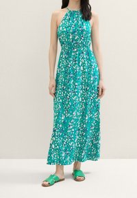 Abito maxi in teal con stampa astratta multicolore. Presenta un collo all'americana, vita arricciata e un design fluido. Abbinato a sandali verdi con fasce.