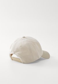 Gorra de béisbol beige con visera curva, tela texturizada y correa ajustable en la parte posterior que presenta agujeros espaciados uniformemente para personalización.