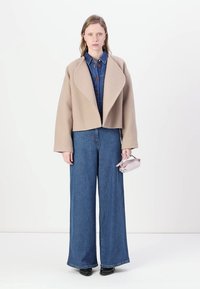 Bežna, skrajšana jakna iz volnene mešanice z širokimi reverji, nosena čez jeans kombinezon; model drži majhno, svetlo roza torbico; modri široki kavbojke.