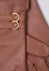 Brown leather gloves featuring two gold-tone circular buckles, stitched details, and a textured finish. Smooth interior with fitted shape.