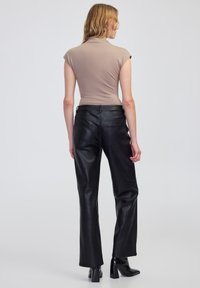 Brązowa dopasowana bluzka z krótkimi rękawami, zestawiona z czarnymi, skórzanymi spodniami o wysokim stanie, z tylnymi kieszeniami i prostymi nogawkami.