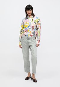 Chemise à manches longues avec des imprimés graphiques multicolores, associée à un jean gris clair et des chaussures noires brillantes avec un détail nœud.